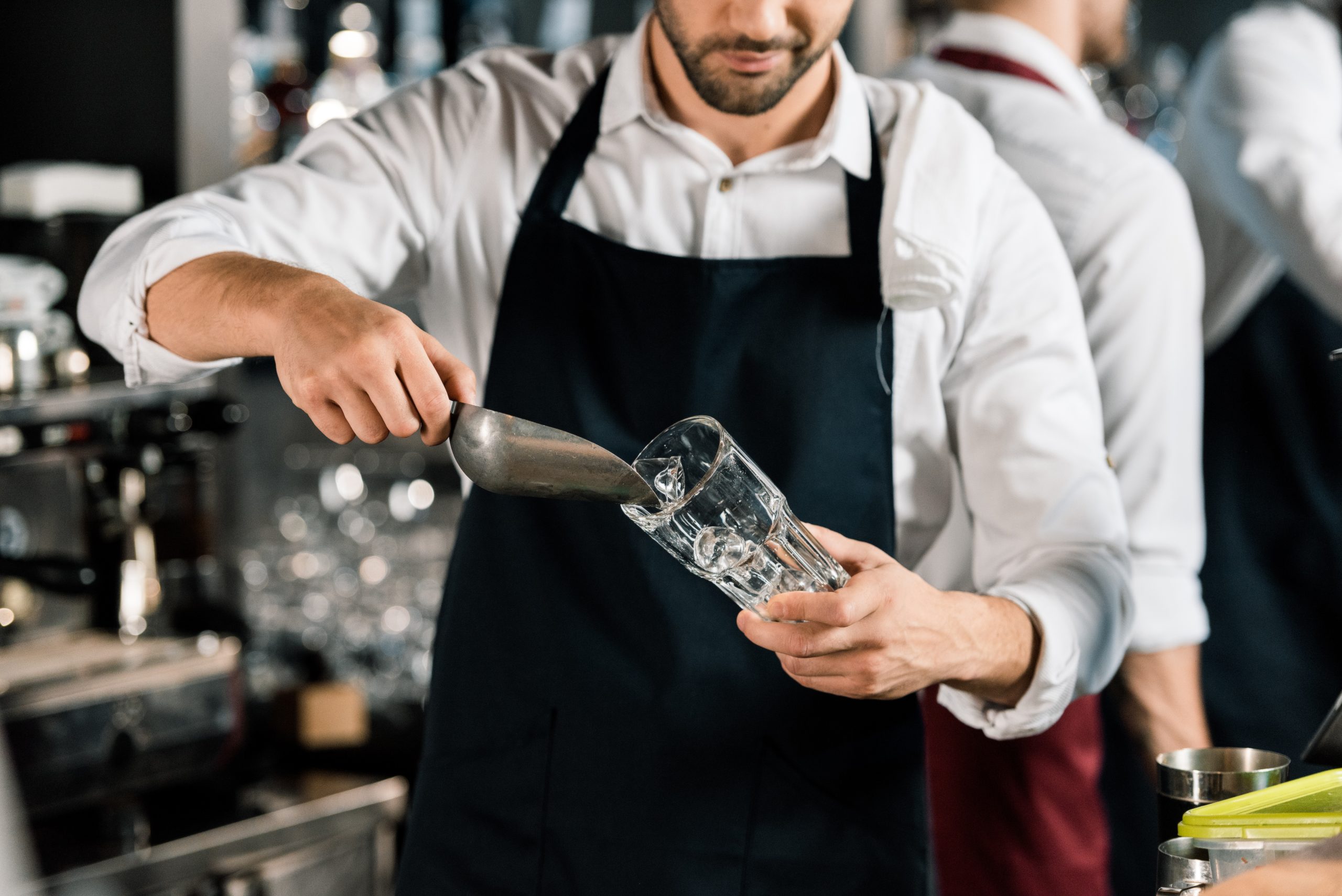 cropped view of barman in apron putting ice in glass