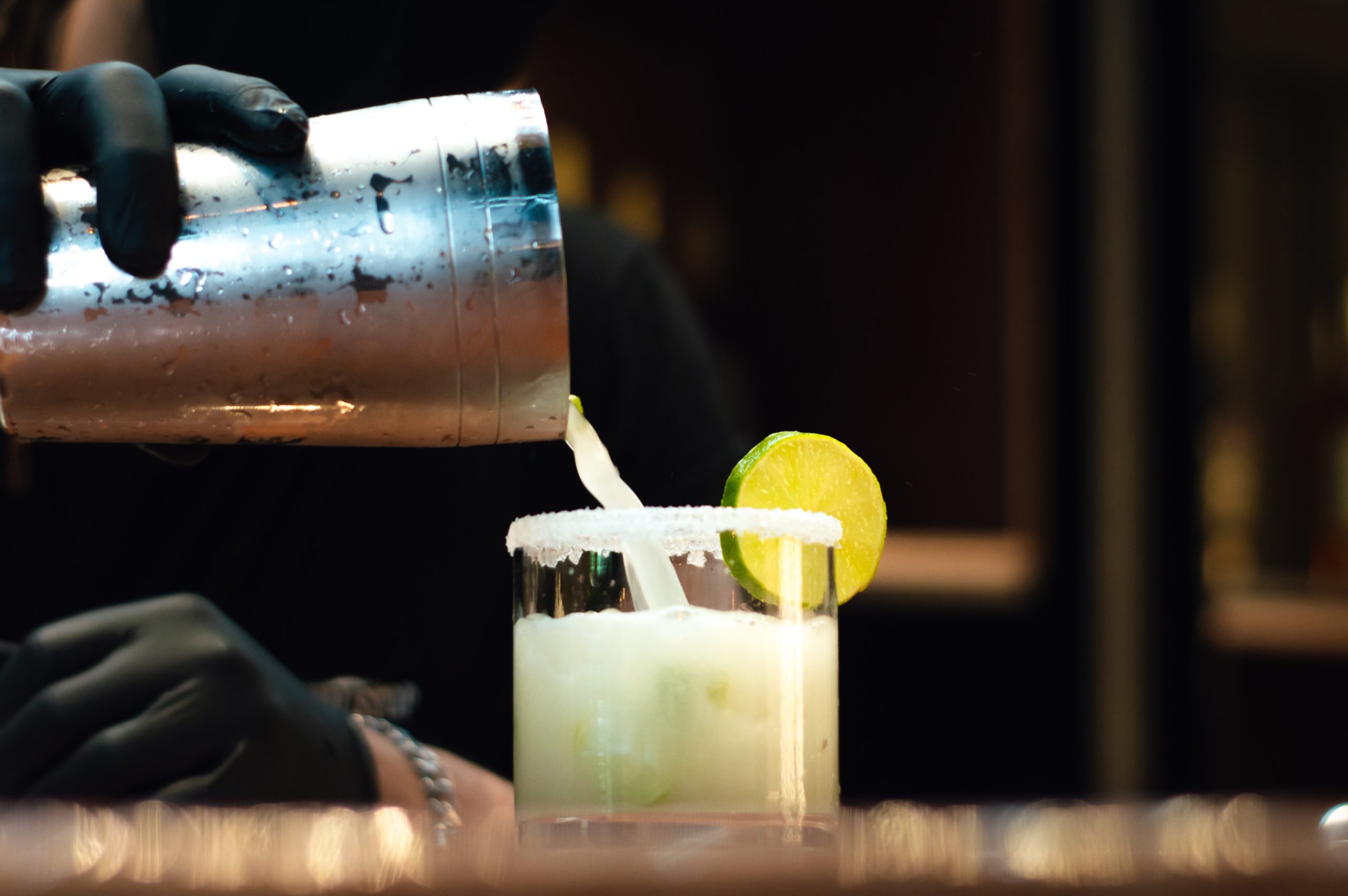 bartender pouring drink on a glass with a lime